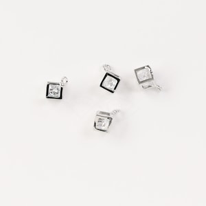 May include: Four silver-toned metal charms with clear cubic zirconia stones. Each charm features a square shape with a small loop at the top for attaching to jewelry.