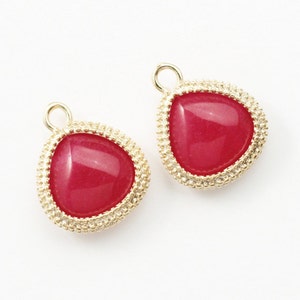 Puede incluir: Dos colgantes de color dorado en forma de lágrima con un centro de piedra rosa y un borde de cuentas.