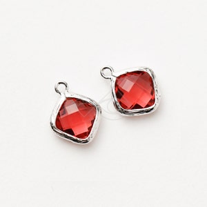 May include: Two silver charm pendants with red square-shaped glass stones. The stones have a faceted design.