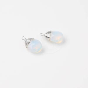 Op de afbeelding: Twee witte opaal hangers met zilveren draad gewikkeld. De opalen zijn ovaalvormig en hebben een doorschijnende, melkachtig witte kleur.