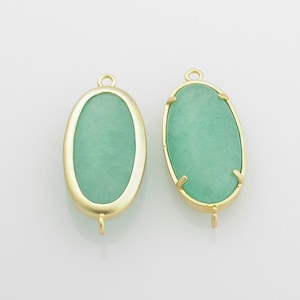 May include: Two gold oval-shaped pendant charms with a green stone inlay. The charms have a loop at the top for attaching to a necklace or bracelet.