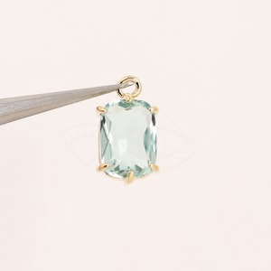 May include: A gold pendant featuring a light blue gemstone in a rectangular shape.