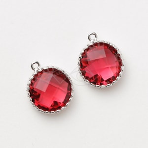 Puede incluir: Dos abalorios plateados con piedras de cristal facetadas rojas. Cada abalorio tiene un borde decorativo.