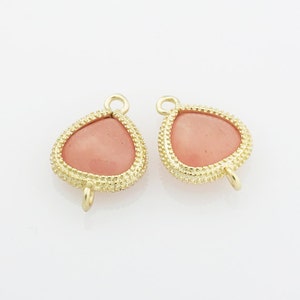 May include: Two gold-tone pendant charms with a pink teardrop-shaped stone set in a textured bezel. Each charm has a loop at the top and a jump ring at the bottom.