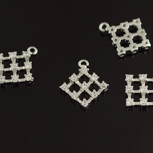 May include: Four silver-toned pendant charms with a square grid design. Each charm is adorned with clear rhinestones.