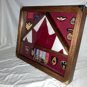May include: A wooden display case featuring a Canadian flag, military medals, and various patches. The flag is red and white, and the case has a dark wood finish with brass corner detailing. The interior is lined with red fabric.