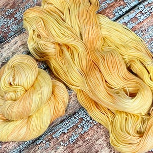 May include: A skein of yellow and orange hand-dyed yarn. The yarn is soft and fluffy, and it has a subtle ombre effect.