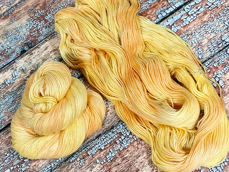 May include: A skein of yellow and orange hand-dyed yarn. The yarn is soft and fluffy, and it has a subtle ombre effect.