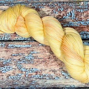 May include: A skein of yellow and orange hand-dyed yarn. The yarn is soft and fluffy, and it would be perfect for knitting or crocheting a cozy scarf or blanket.