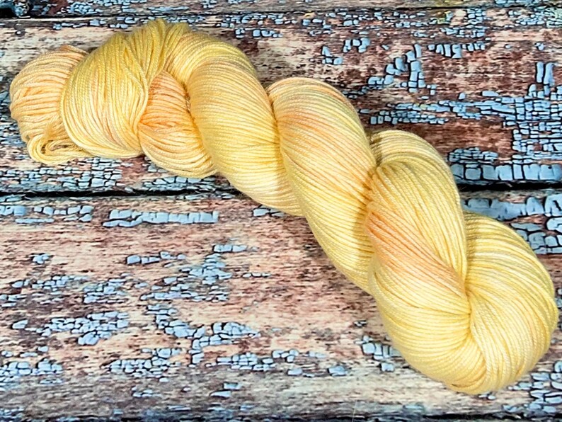 May include: A skein of yellow and orange hand-dyed yarn. The yarn is soft and fluffy, and it would be perfect for knitting or crocheting a cozy scarf or blanket.