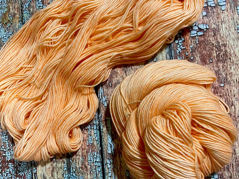 May include: A close-up of two skeins of peach-colored yarn. The yarn is soft and fluffy, and it is perfect for knitting or crocheting.