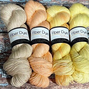 May include: Four skeins of hand-dyed yarn in shades of beige, peach, yellow, and bright yellow. The yarn is labeled "Fiber Dyed" with the company's contact information.