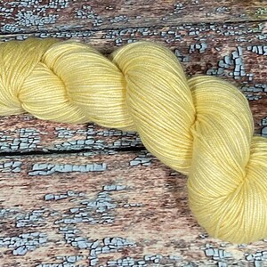 May include: A skein of soft, yellow yarn. The yarn is loosely wound and has a subtle sheen.