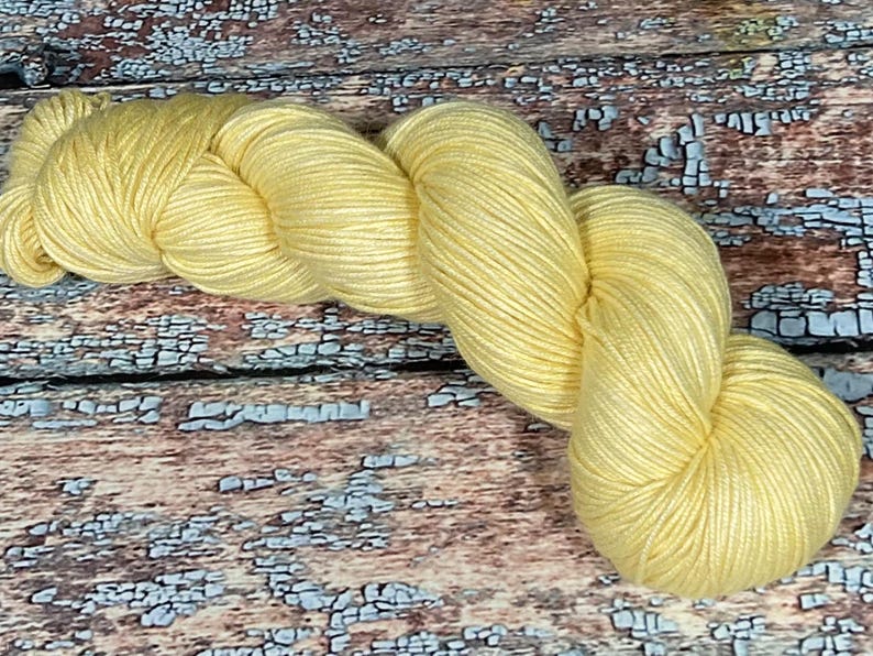 May include: A skein of soft, yellow yarn. The yarn is loosely wound and has a subtle sheen.