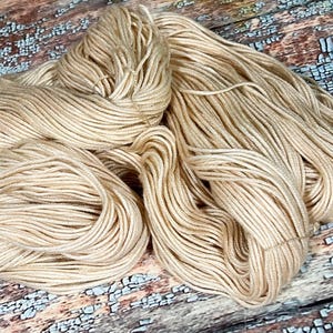 May include: A skein of beige yarn, a soft and natural color, perfect for knitting or crocheting.