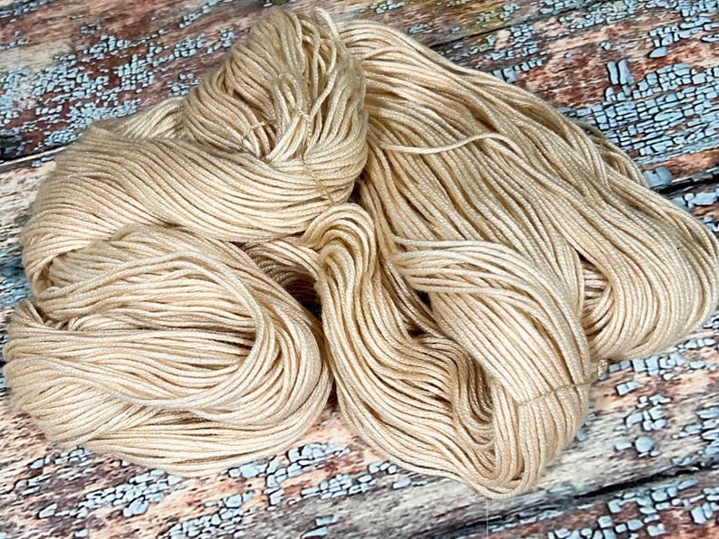 May include: A skein of beige yarn, a soft and natural color, perfect for knitting or crocheting.