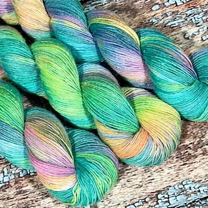 May include: A skein of yarn with a multi-colored pattern of teal, green, yellow, pink, and white. The yarn is twisted and folded, showing the different colors.
