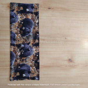 May include: A black and brown fabric runner with a repeating pattern of black bears. The bears are lying down and facing different directions.