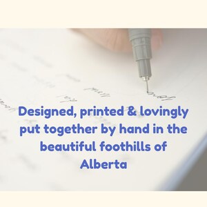 May include: A hand holding a gray pen writing on white paper. The text in the image reads: "Designed, printed & lovingly put together by hand in the beautiful foothills of Alberta."