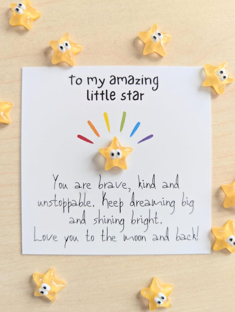 May include: A white card with the text "to my amazing little star" and "You are brave, kind and unstoppable. Keep dreaming big and shining bright. Love you to the moon and back!" surrounded by yellow star-shaped decorations.