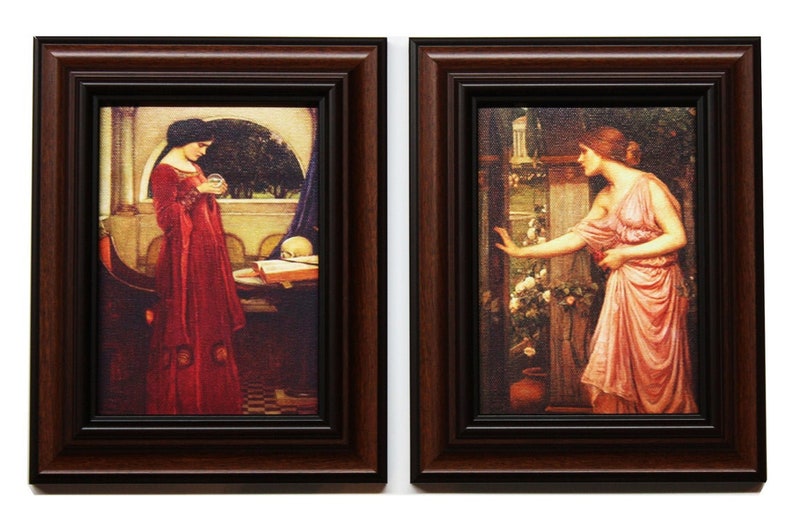 May include: Two framed paintings of women in long dresses. The woman in the left painting is holding a crystal ball and a book. The woman in the right painting is reaching out with her hand. Both paintings have a dark brown frame.