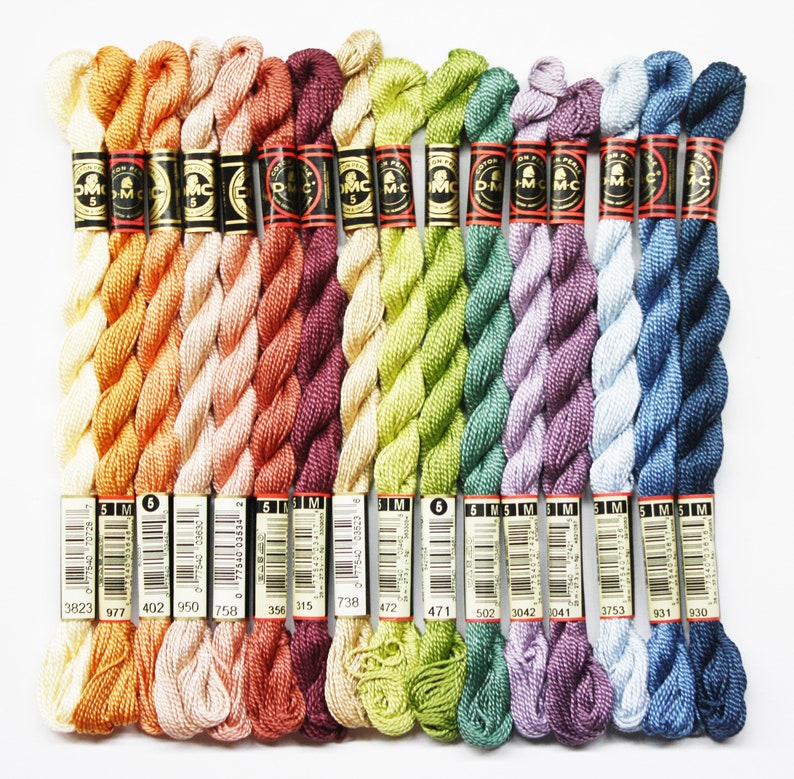 May include: A collection of 15 skeins of DMC embroidery floss in various shades of orange, peach, red, green, purple, blue, and gray. Each skein is labeled with the DMC color number and is wrapped in a black and gold label.