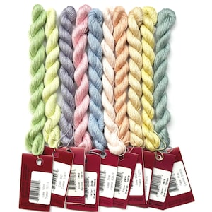 May include: A collection of embroidery floss in various pastel colors, including green, yellow, pink, and blue. Each skein is labeled with a red tag, displaying color and dye lot information. The floss is arranged vertically against a white background.