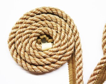 May include: A close-up of a coiled beige rope with a white plastic end cap. The rope is made of a thick, twisted cord and has a subtle sheen.