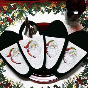 May include: Set of four black and white Santa Claus themed fabric place card holders. Each holder features a Santa Claus face with a red hat and white beard. The holders are on a white surface with a red and green holiday tablecloth.