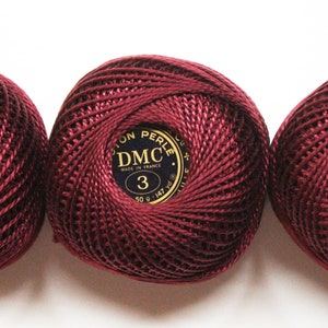 May include: Three spools of maroon DMC Cotton Perle embroidery floss, each with a gold label that reads "DMC Cotton Perle 3 Made in France 50 g - 1.75 oz - 147 yds - 134 m".