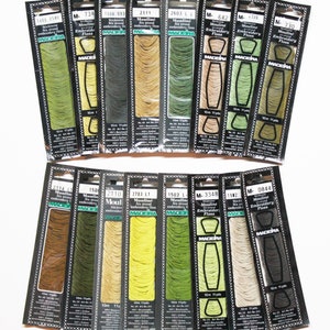 May include: A collection of 12 spools of Madeira embroidery floss in various shades of green, brown, and beige. Each spool is labeled with the brand name, color number, and length in meters and yards.