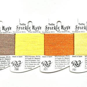 May include: Four cards of Petite Sparkle Rays embroidery thread in metallic copper, bright yellow, vibrant orange, and pale yellow. Each card contains 10 yards of 96% polyester and 4% nylon thread, labeled with product codes PS44, PS80, PS77, and PS51.