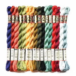 May include: A collection of 15 spools of DMC embroidery floss in various shades of blue, green, red, orange, and yellow. The spools are labeled with DMC numbers and are arranged in a row.