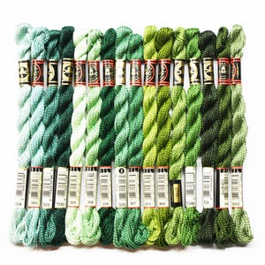 May include: A collection of green embroidery floss skeins, arranged in rows. The floss colors range from light teal to dark forest green. Each skein is labeled with a number and brand information.