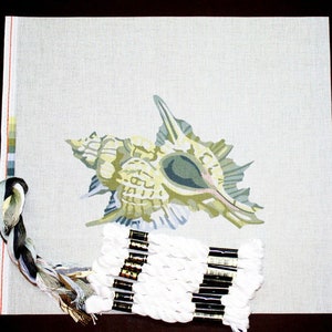 May include: A needlepoint canvas with a printed design of a seashell. The canvas is beige with a light green seashell design. A skein of white embroidery floss is included.
