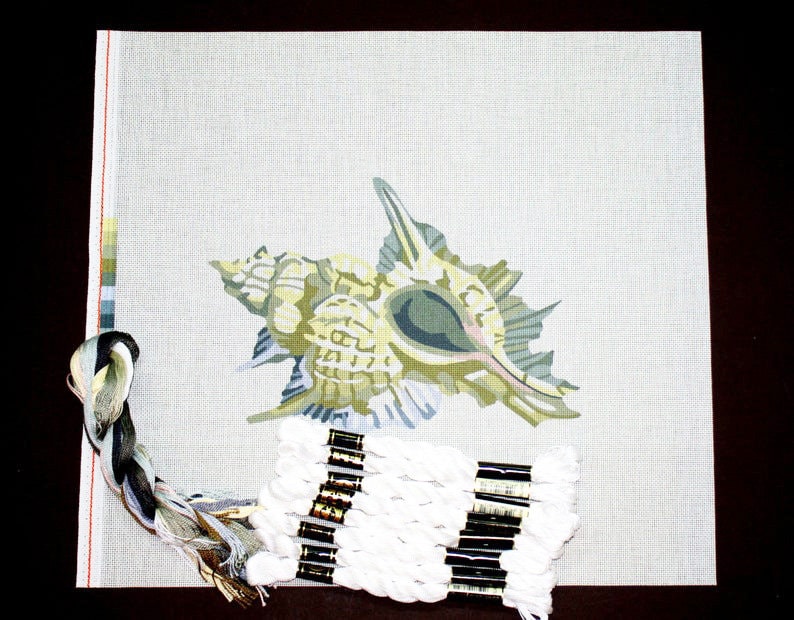 May include: A needlepoint canvas with a printed design of a seashell. The canvas is beige with a light green seashell design. A skein of white embroidery floss is included.
