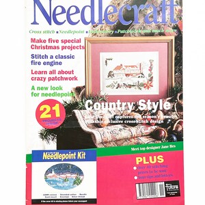 May include: A magazine cover for Needlecraft magazine, featuring a cross-stitch design of a country scene with a house, trees, and snow. The cover text reads "Country Style" and "21 Projects Inside".