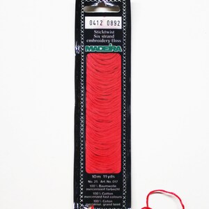May include: A package of red Madeira Sticktwist six-strand embroidery floss. The black label displays the product information, including the length of 11 yards. A strand of the red floss is loose.