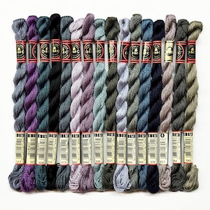 May include: A collection of 18 DMC embroidery floss spools in various shades of purple, green, gray, and brown. The spools are labeled with the DMC numbers 317, 327, 924, 310, 413, 3042, 3041, 926, 3021, 318, 645, 930, 939, 451, 344, and 640.