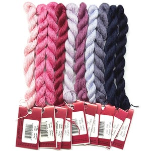 May include: A collection of embroidery floss in various shades of pink, purple, and blue. The floss is arranged in neat bundles, each with a color tag attached. The tags display color codes and dye lot information. Ideal for embroidery and other needlecraft projects.