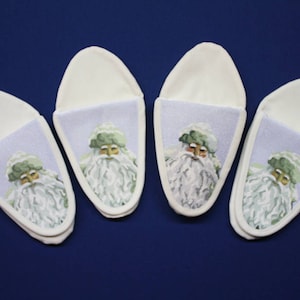 May include: Four pairs of white slipper socks with a light blue interior. Each slipper sock features a cartoon image of Santa Claus with a white beard and green hat.
