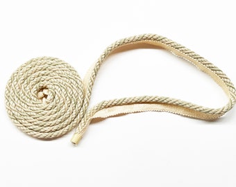 May include: A beige and white braided rope trim with a coiled section. The trim is made of a soft, woven fabric and has a subtle sheen.