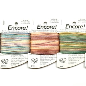 May include: Five spools of Encore! medium strandable 4-ply cotton thread in various colors. Each spool is labeled with a unique code and features a white label with the brand name and product details. Ideal for needlepoint and cross-stitch.
