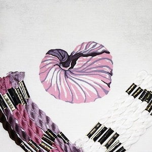 May include: A white canvas with a pink and purple nautilus shell design. The canvas is surrounded by spools of embroidery floss in shades of pink, purple, and white.