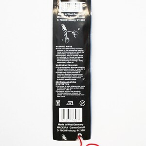 May include: Black packaging for embroidery thread with red thread extending from the bottom. The packaging has text in multiple languages, including washing instructions. The packaging is from Madeira Garne GmbH, Made in West Germany.