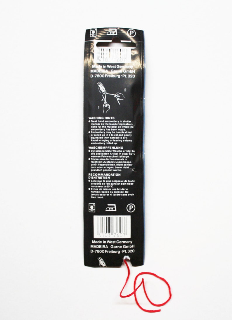 May include: Black packaging for embroidery thread with red thread extending from the bottom. The packaging has text in multiple languages, including washing instructions. The packaging is from Madeira Garne GmbH, Made in West Germany.