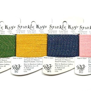 May include: Four spools of Sparkle Rays thread in green, gold, navy blue, and pink. Each spool is labeled with the brand name and details, including the material and length of 10 yards (9.1 meters).