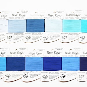 May include: A collection of 12 spools of Neon Rays needlepoint ribbon in various shades of blue. Each spool is labeled with the brand name, color number, and length. The ribbon is made of 100% rayon and is hand washable.