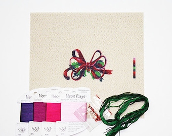 May include: A cross stitch kit featuring a red and green bow with holly leaves. The kit includes a piece of Aida cloth, embroidery floss, beads, and ribbon.