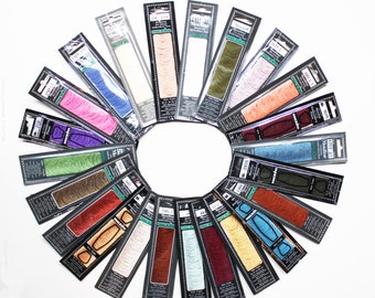 May include: A circular arrangement of embroidery floss in various colors, including pink, purple, green, and blue. Each skein is packaged in a black and white sleeve with product information. The floss is arranged on a white surface.